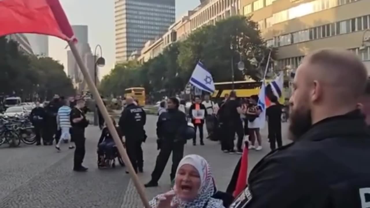 Elderly Woman Rocks While Chaos Unfolds Behind Her in Germany's Genocide Scene