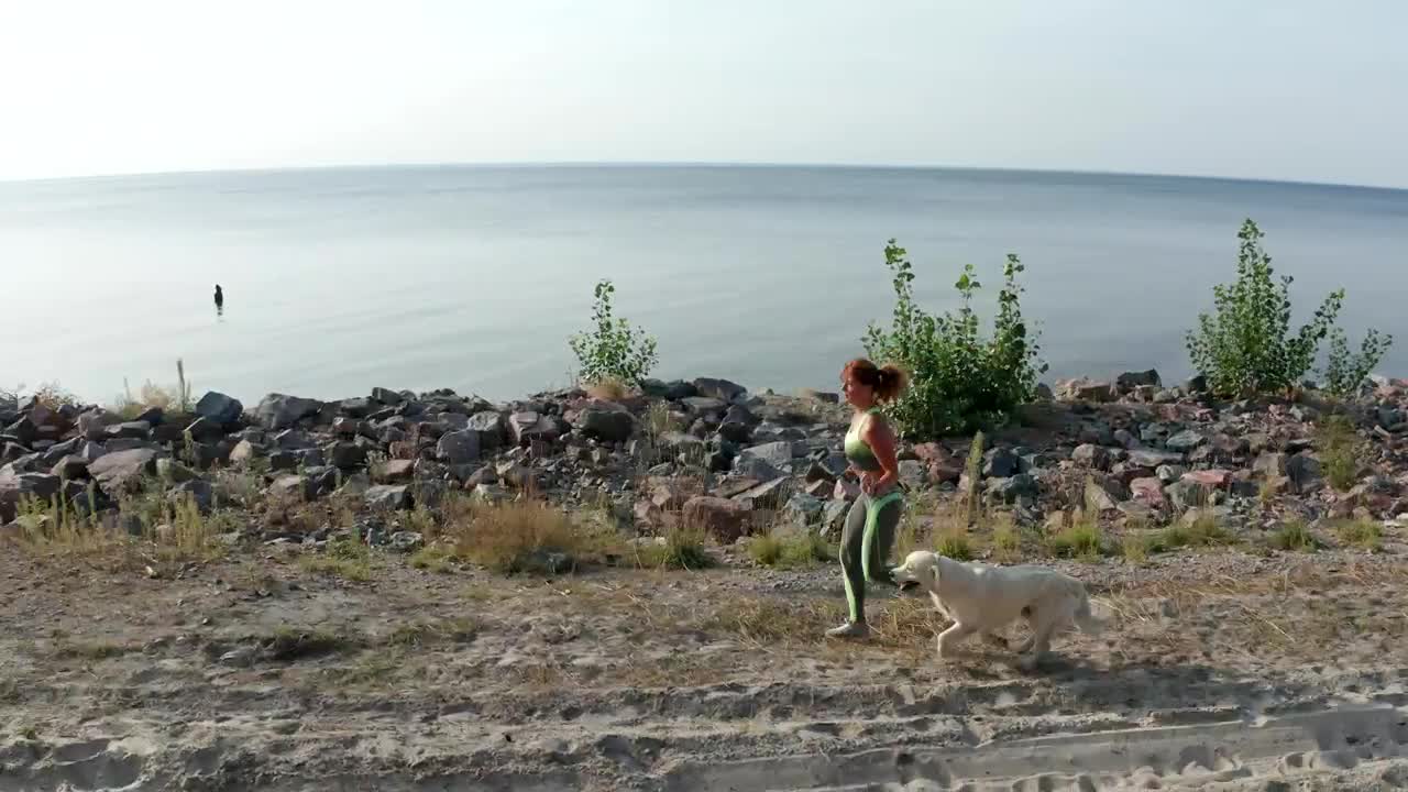 Young woman running with her dog near a coast