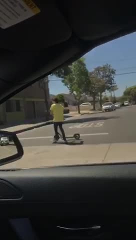 Kid yellow shirt using bird electric scooter while riding skateboard
