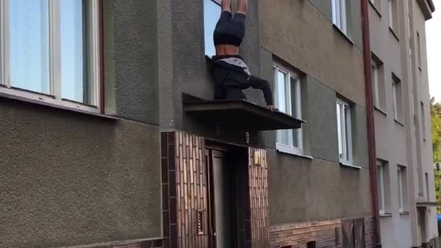 Guy does handstand on awning in front of apartment