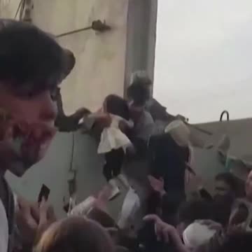 A little Afghan girl is lifted over the wall to U.S. soldiers amid chaos and crowds Kabul airport.