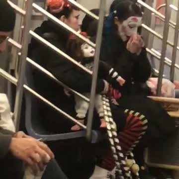 Guy smiles at camera, people dressed as circus clowns sit in the background on subway train
