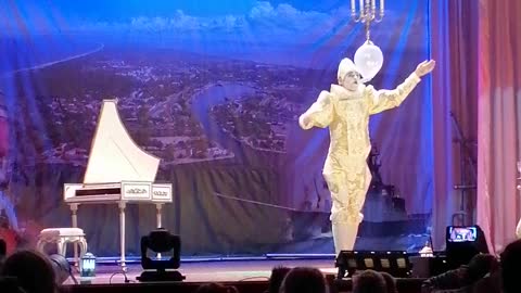 A juggler plays the piano with glasses in his mouth.