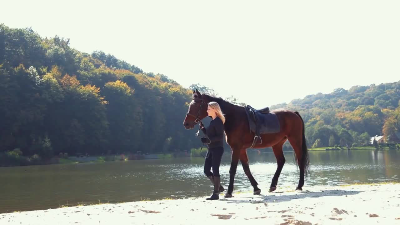 blonde jockey girl with horse near lake