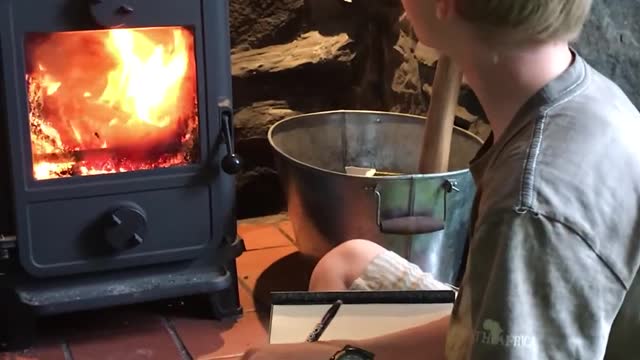 Kid Concentrates on Writing Inside His Notebook While Sitting Next to Fire