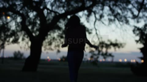 A woman runs in a field near a tree in the evening