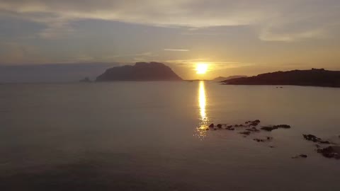 Porto Istana, Olbia, Sardegna. Drone dalla spiaggia verso Tavolara con sole che sorge