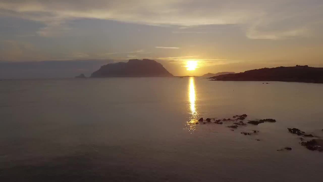 Porto Istana, Olbia, Sardegna. Drone dalla spiaggia verso Tavolara con sole che sorge