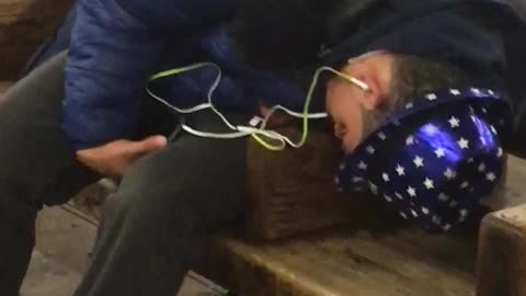 Man with blue hat lights asleep on subway bench