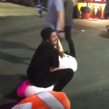 Guy riding unicorn stuffed animal at fair