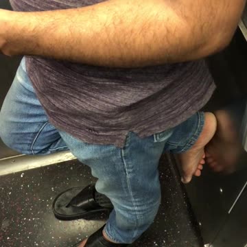 Man has one sandal on and bare foot on wall of subway