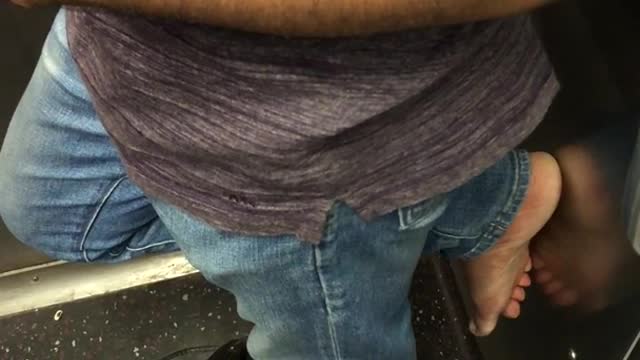 Man has one sandal on and bare foot on wall of subway