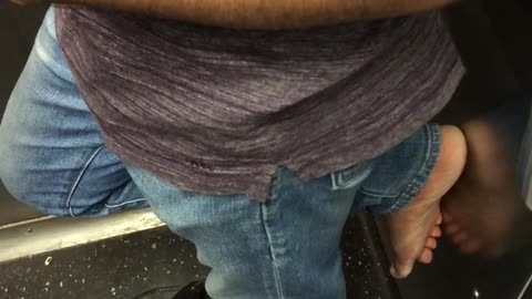 Man has one sandal on and bare foot on wall of subway