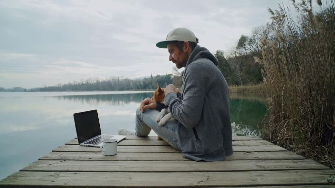 Static shot of hipster man in hoodie and cap with best friend puppy on lap, cuddle and pet his dog