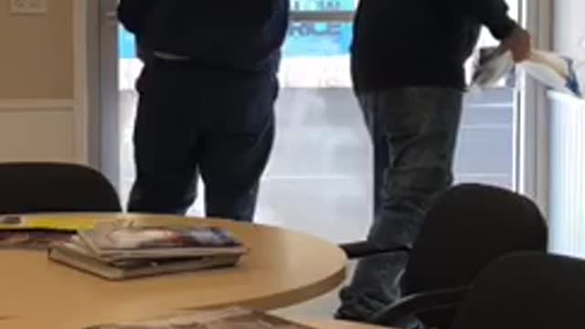 Guy wipes his hand on window after his friend is almost done cleaning it