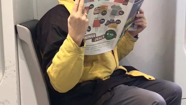 Yellow jacket man reads newspaper very close to face on subway