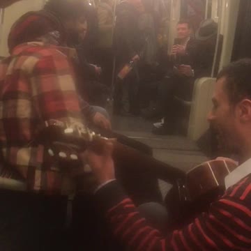 Man in red flannel and man with guitar singing on train