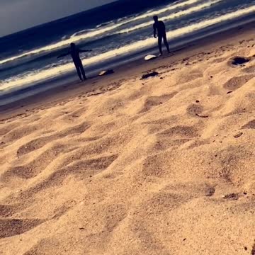 Guy narrates two guys in wetsuits warming up on beach before surfing