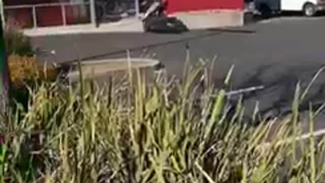 Guy does a wheelie on his motorcycle in a parking lot and crashes into motorcycle store wall