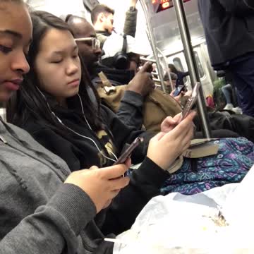 Girl eats asada fries on subway train, girl next to her texts on her phone