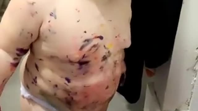 Toddler splattered with paint looks pleased (paint!)