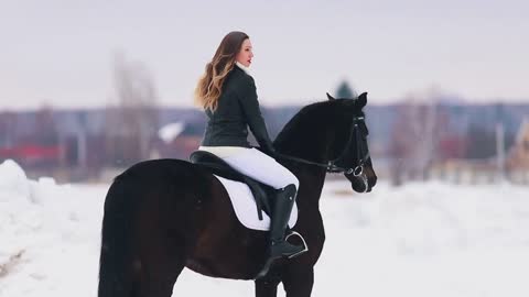 A happy young woman with long hair riding a horse in a village. Standing on snowy ground