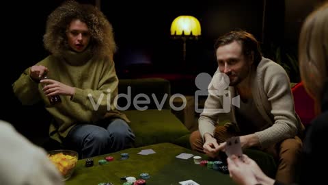 Group Of Friends Playing Poker Sitting On The Coach In The Living Room