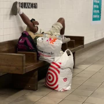 Man lays down and stretches his legs on subway station bench
