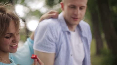 Young guy and beautiful girl play with their pet in the park. A guy is feeding a dog a strawberry
