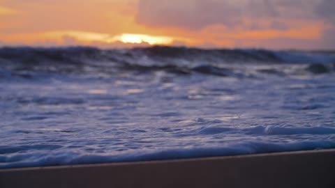 Handheld closeup of waves on echo beach shore at sunset