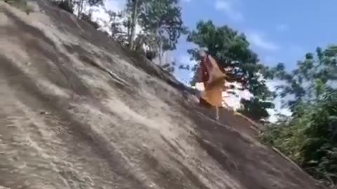 A monk climbing with bare feet on the cliff that tourists climb on with the help of a rope