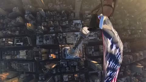 Guy waving American Flag at the top of a building.