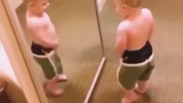 A child displays his His muscles in front of the glass mirror