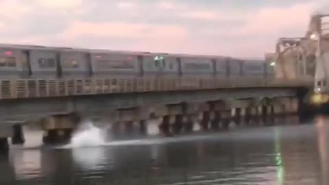 Two people jump from moving train on bridge to water below