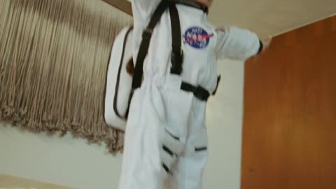 Little girl dressed as an astronaut jumping on the bed