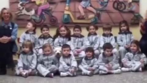 Small white dog sits in picture with classroom of kids