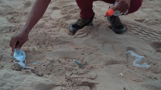 A guy picking up plastic and other trash from the sand on the beach_batch