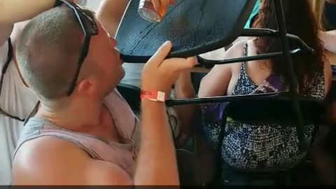 Guy in red tank top does beer luge off of a plastic black chair