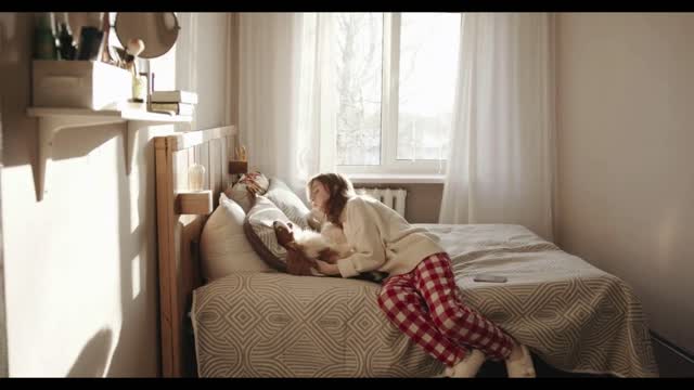 A cheerful young girl plays with her dog while sitting on the bed