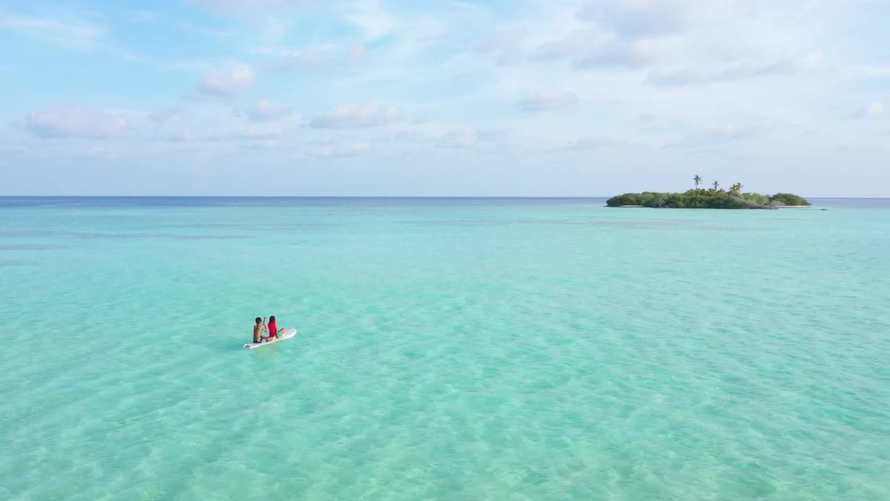 A couple seated on a paddle board in the sea