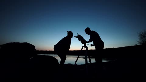 Silhouettes of people using a telescope at dusk