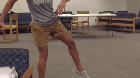Guy with khaki shorts and grey shirt does kick spins in middle of class room and loses glasses and lands on butt
