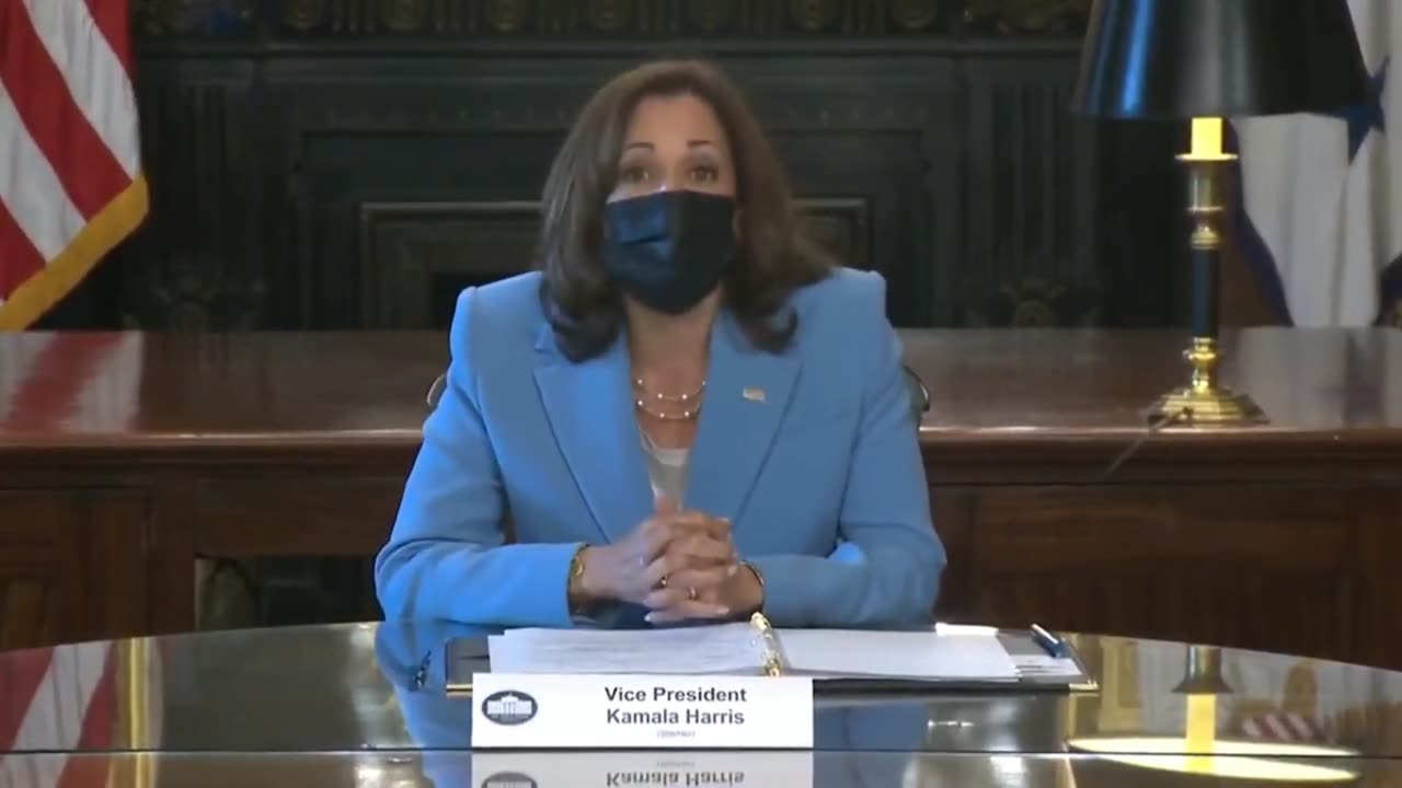 She Is A Woman Sitting At A Table Wearing A Blue Suit