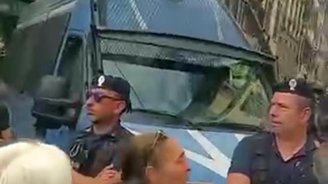 Cops in Italy surrounded by people holding up photos of vaccine victims