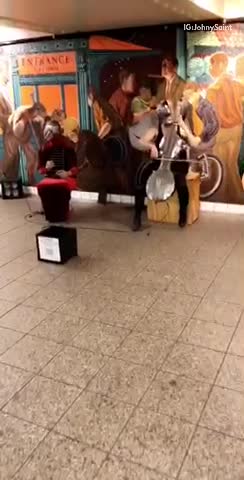 Two people in silver masks playing instruments in subway station
