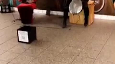 Two people in silver masks playing instruments in subway station