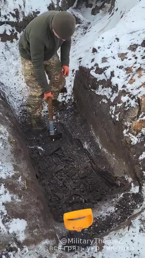 Ukrainian soldier using an axe to dig a trench
