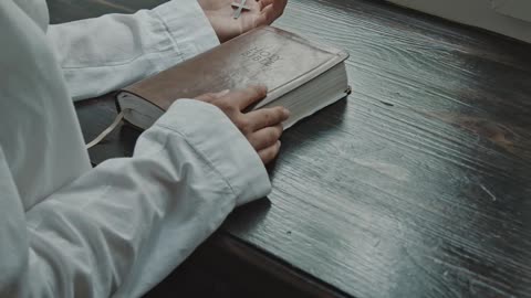 WOMAN HOLDING A BIBLE AND CROSS WHILE PRAYING BY THE WINDOW