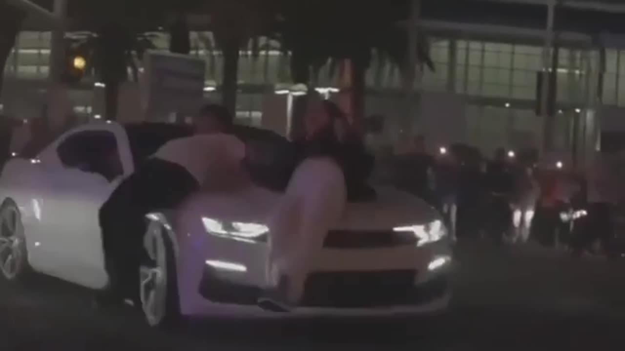 car hits a couple in crowd but they slide off perfectly and go about their shady affairs.