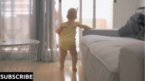 Back view of one year old baby girl walking at home leaning on the sofa